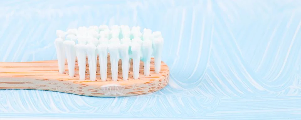 Bamboo toothbrush with toothpaste on the left on a soft blue background 스톡 사진