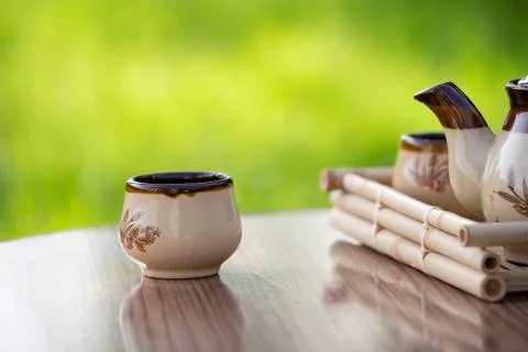 Bamboo tray, patterned teapot and cups in garden. Blurry green background Stock Photos