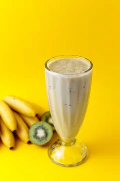 Banana and kiwi milkshake in glass with kiwi and bananas on yellow background Stock Photos