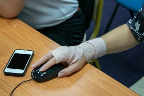 Bandaged Hand Using Computer Mouse at Desk Stock Photos