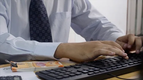 A banker counting Indian currency notes and making entry in his computer Stock Footage 114812583