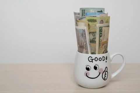Banknotes from different countries in a white coffee mug. Stock Photos