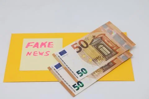 Banknotes in a yellow envelope on a light background. Fake news sticker on th Stock Photos