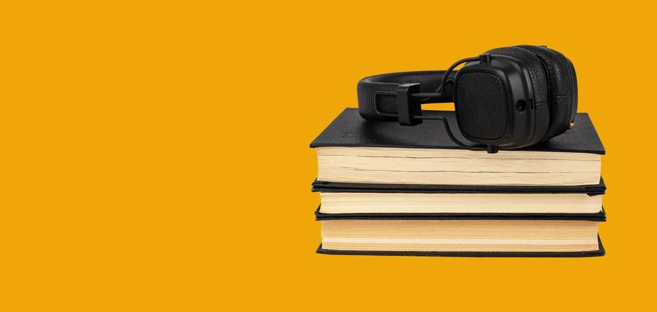 Banner with headphones on books stack on orange background. Listening to audi Stock Photos