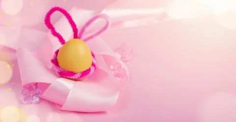 Banner with a yellow Easter egg with pink bunny ears and satin ribbon Stock Photos
