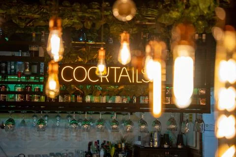 Bar interior featuring illuminated cocktail sign with hanging light bulbs, Фото