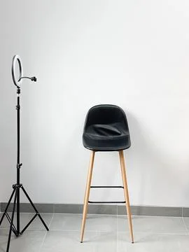 Bar stool and a ring lamp against a white wall - a stylish setup for video sh Stock Photos