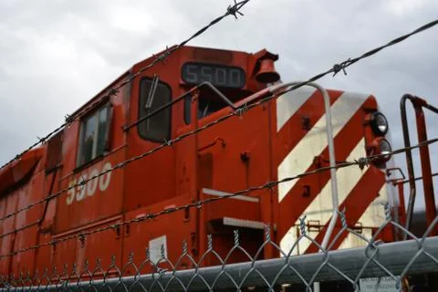 Barb-wired fence with train engine in yard Stock Photos