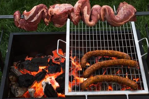 Barbecue with beef inserted in a sword and some sausages on a grill grilling Stock Photos