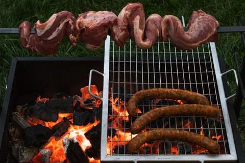 Barbecue with beef inserted in a sword and some sausages on a grill grilling  Stock Photos