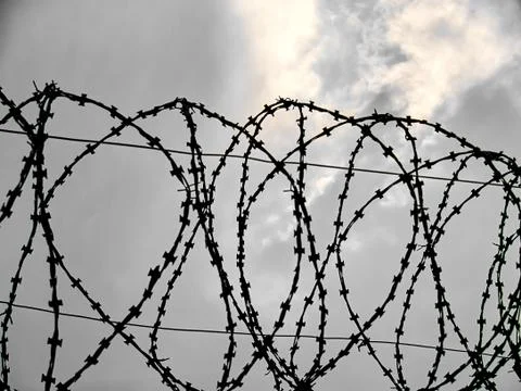Barbed wire against the background of clouds through which sunlight breaks th Stock Photos