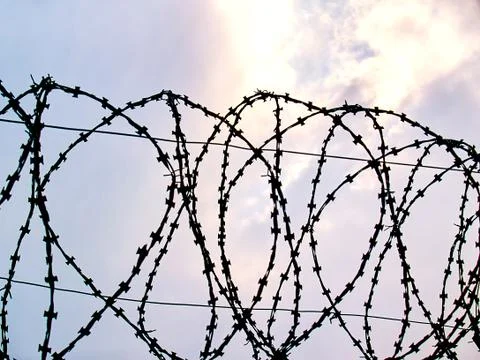 Barbed wire against the background of clouds through which sunlight breaks th Stock Photos