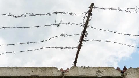 Barbed wire against the sky. A security fence on the territory of a prison or Stock Photos