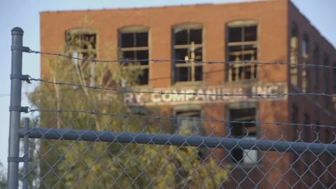 Barbed wire and chain link fence, brick building in background 库存影片 304373447
