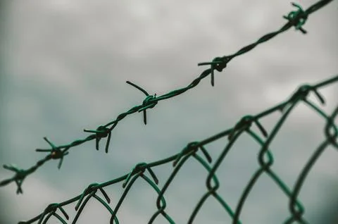 Barbed wire and chain link fence against sky Stock Photos