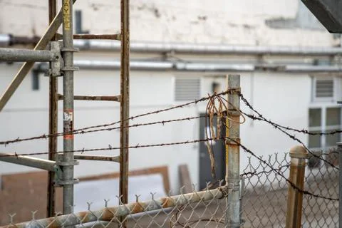Barbed wire and dirty string on top of rusty fence blocking entrance to building Stock Photos