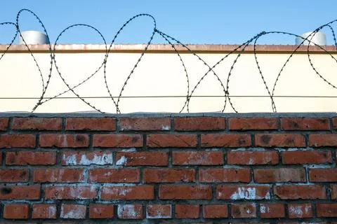 Barbed wire with brick wall and light building in the background against the Stock Photos