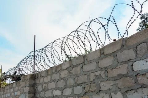 Barbed wire on brick wall or fence in front of blue sky. Concept of security  스톡 사진