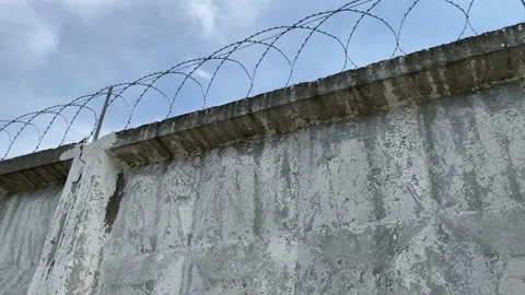 Barbed wire on a concrete prison wall with cracked white plaster Stock Footage 154189917