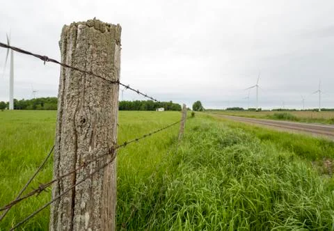 Barbed wire fence along a country road with green grass fields Stock Photos