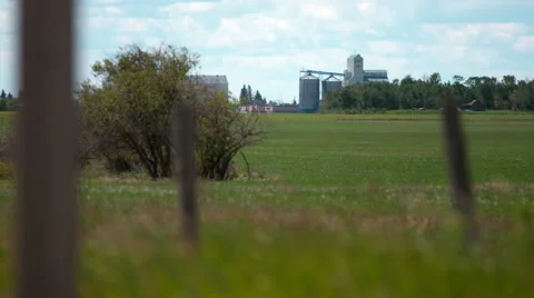 Barbed wire fence with grass in foreground of agricultural storage facility Stock Footage 67612697