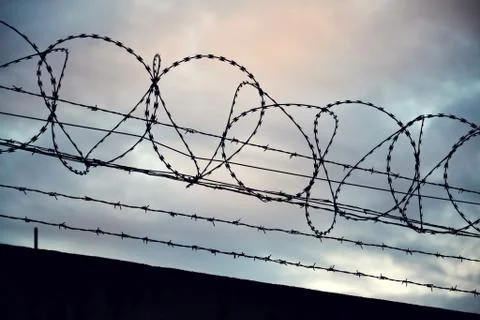 Barbed wire fence layed around prison walls Stock Photos