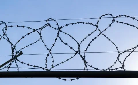 Barbed wire fence of the protected object against the sky close-up Stock Photos