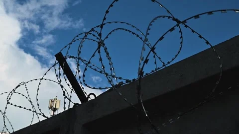 Barbed wire fencing against a backdrop of blue sky and clouds, illustrating a Vídeos de archivo 344527798