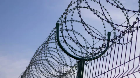 Barbed wire Hanging on the Border of Iron Fence on Against the Blue Sky. 4K Video stock 154693397