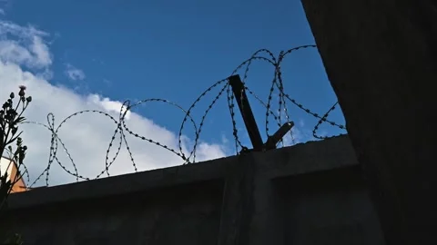 Barbed wire is installed at the top of a wall under a blue sky with clouds. The Vídeo Stock 344527796