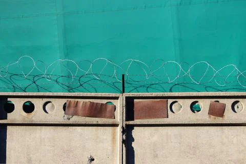 Barbed wire on an old concrete wall guards an object against a green awning Stock Photos