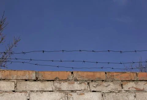 Barbed wire over old brick wall against the sky. Stock Photos