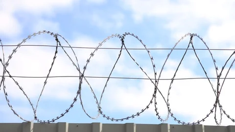 Barbed wire, razor wire on top of steel fence on blue sky background. Video stock 126552327
