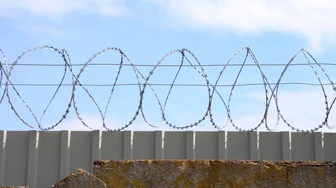 Barbed wire, razor wire on top of steel fence on blue sky background. Video stock 126552353