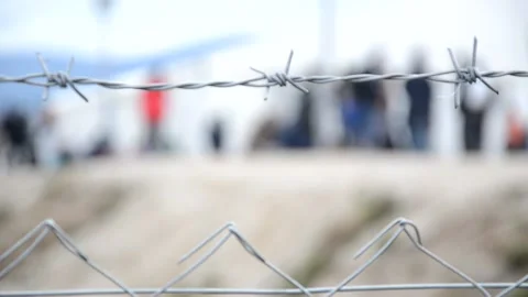 Barbed wire in refugee camp. Migrants behind chain link fence in camp. Group Stock Footage 159690865