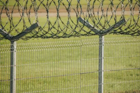 Barbed wire security fence with angled razor wire above metal mesh panels b.. Stock Photos
