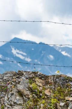 Barbed wire separating the mountain landscape, snowy mountains at background Stock Photos