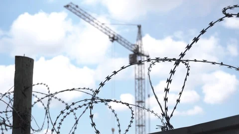 Barbed wire on the territory of the construction site. Crane on sky background Stock Footage 129793113