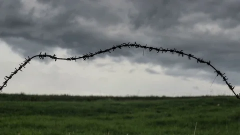 Barbed wire trembling in the wind on the dark stormy clouds background Stock Footage 74344086