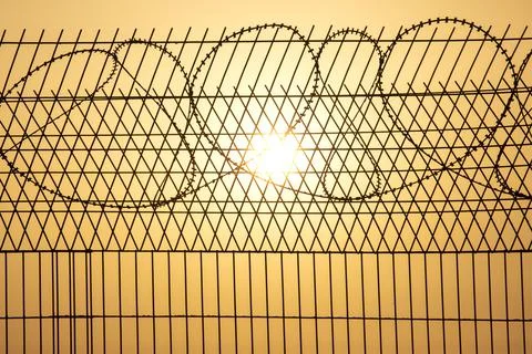 Barbed wire wall against the backdrop of the setting sun. Metaphor of slavery Stock Photos