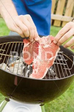Barbeque: man laying t-bone steak on grill Stock Photos
