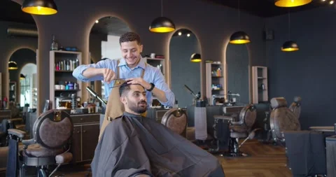 Barber and client, barber prepping, combing and cutting hair with scissors to Stock Footage 337745587