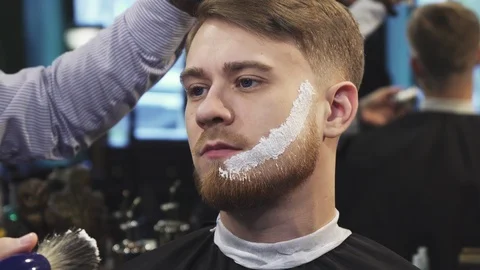 Barber applying shaving cream on the beard of his client Stock Footage 85746734