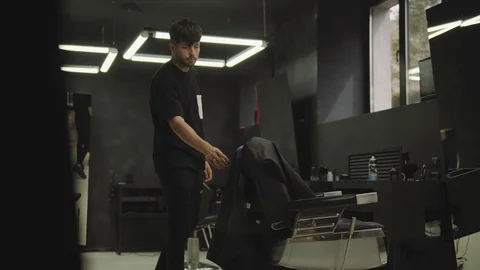 Barber barber prepares for the next client folding a black hair cape in interior Video stock 112831625