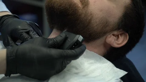 A Barber in black gloves cuts his beard with a shaver Stock Footage 124648864
