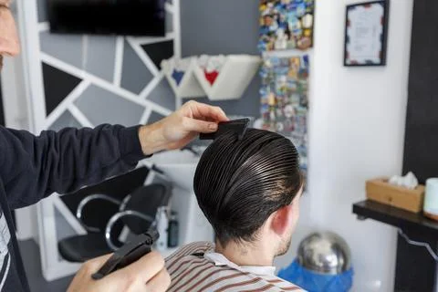 Barber Combing Back of Male Client Hair During Haircut in Modern Barbershop Stock Photos