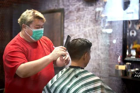 Barber combing the hair of a client while cutting it in a barber shop Stock Photos
