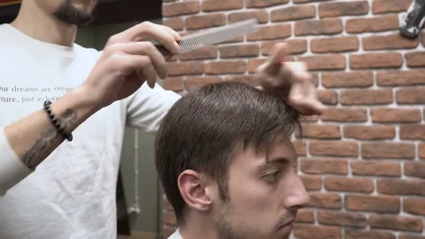Barber combs the comb of a young man in a cape close-up 4k. Stock Footage 81235106
