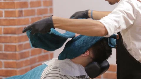 Barber covers the face of a man with a beard with a hot towel. Photo in vintage Stock Footage 93711422