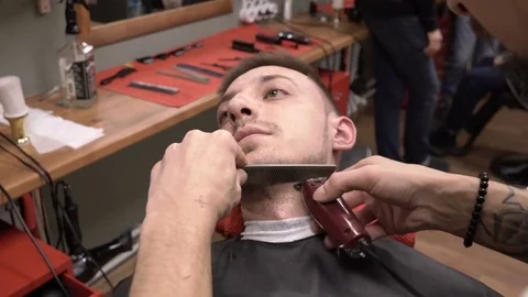 Barber cuts the beard of the client with clipper haircuter and comb close-up 4k. Stock Footage 81547237